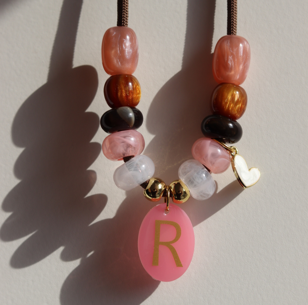 Deze handgemaakte hondenketting 'Rosé glow' is opgebouwd uit een stevig bruin koord met een stijlvolle mix van kralen. Het ontwerp combineert glanzende warmroze, zachtroze en marmerwitte kralen met diepbruine en goudkleurige accenten voor een luxe uitstraling.
