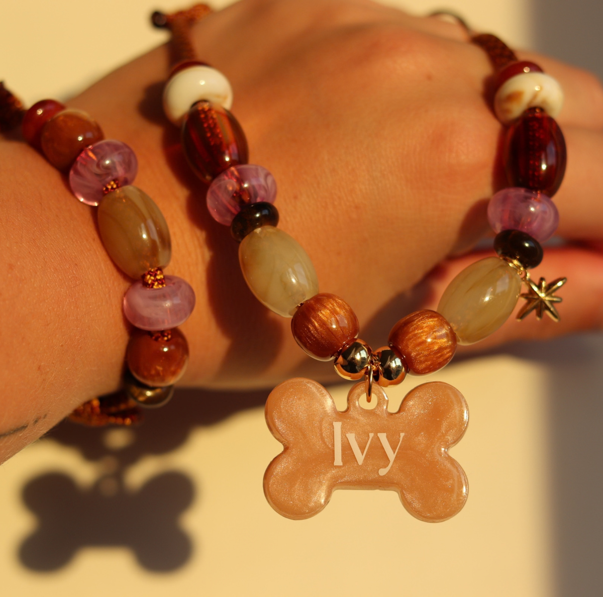 Handgemaakte hondenketting aan een roestbruin koord met amberkleurige en beige kralen, een glinsterend sterretje en een personaliseerbare botvormige naamhanger.