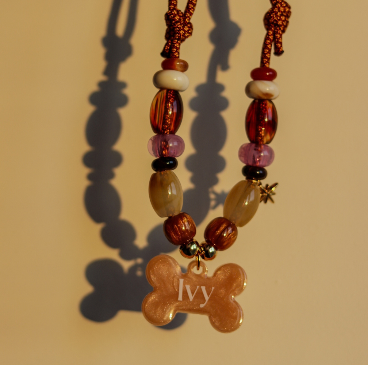 Handgemaakte hondenketting aan een roestbruin koord met amberkleurige en beige kralen, een glinsterend sterretje en een personaliseerbare botvormige naamhanger.