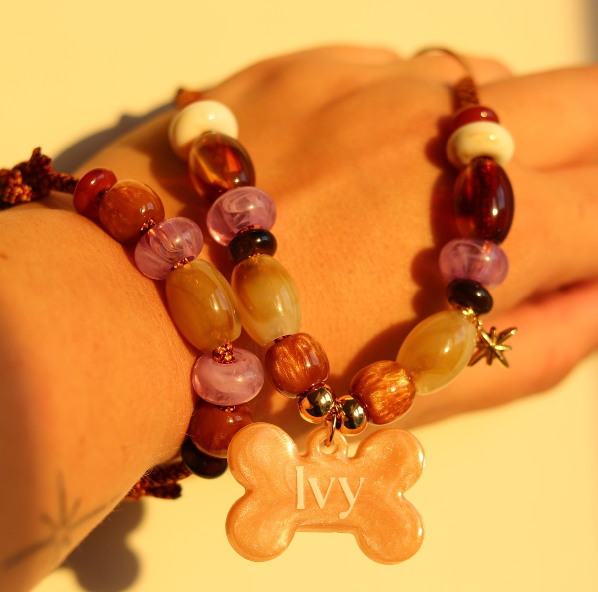Handgemaakte hondenketting aan een roestbruin koord met amberkleurige en beige kralen, een glinsterend sterretje en een personaliseerbare botvormige naamhanger.