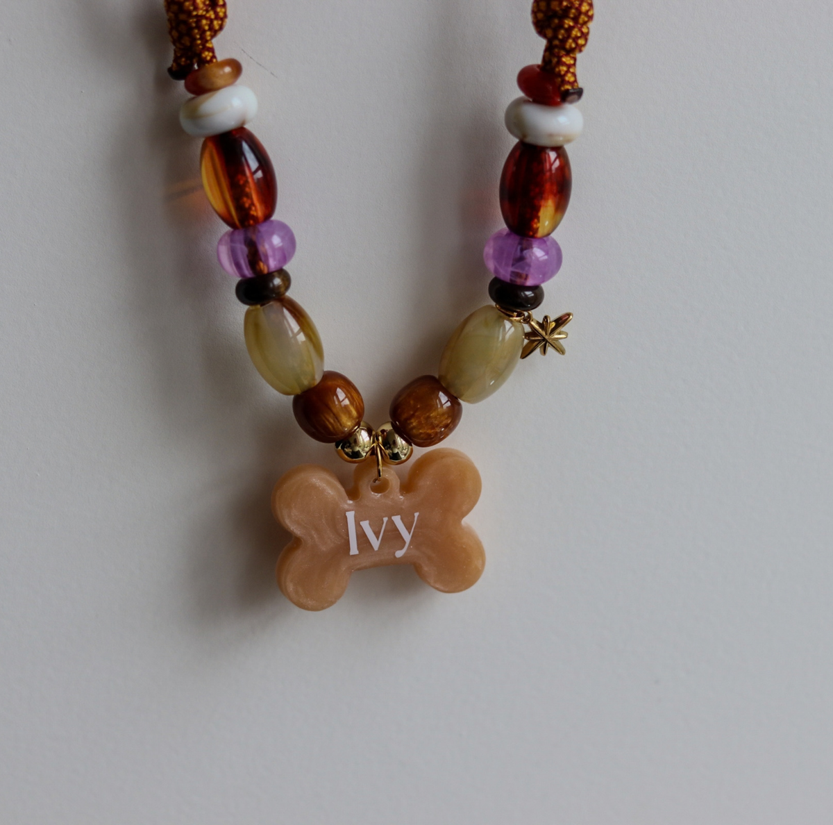 Handgemaakte hondenketting aan een roestbruin koord met amberkleurige en beige kralen, een glinsterend sterretje en een personaliseerbare botvormige naamhanger.