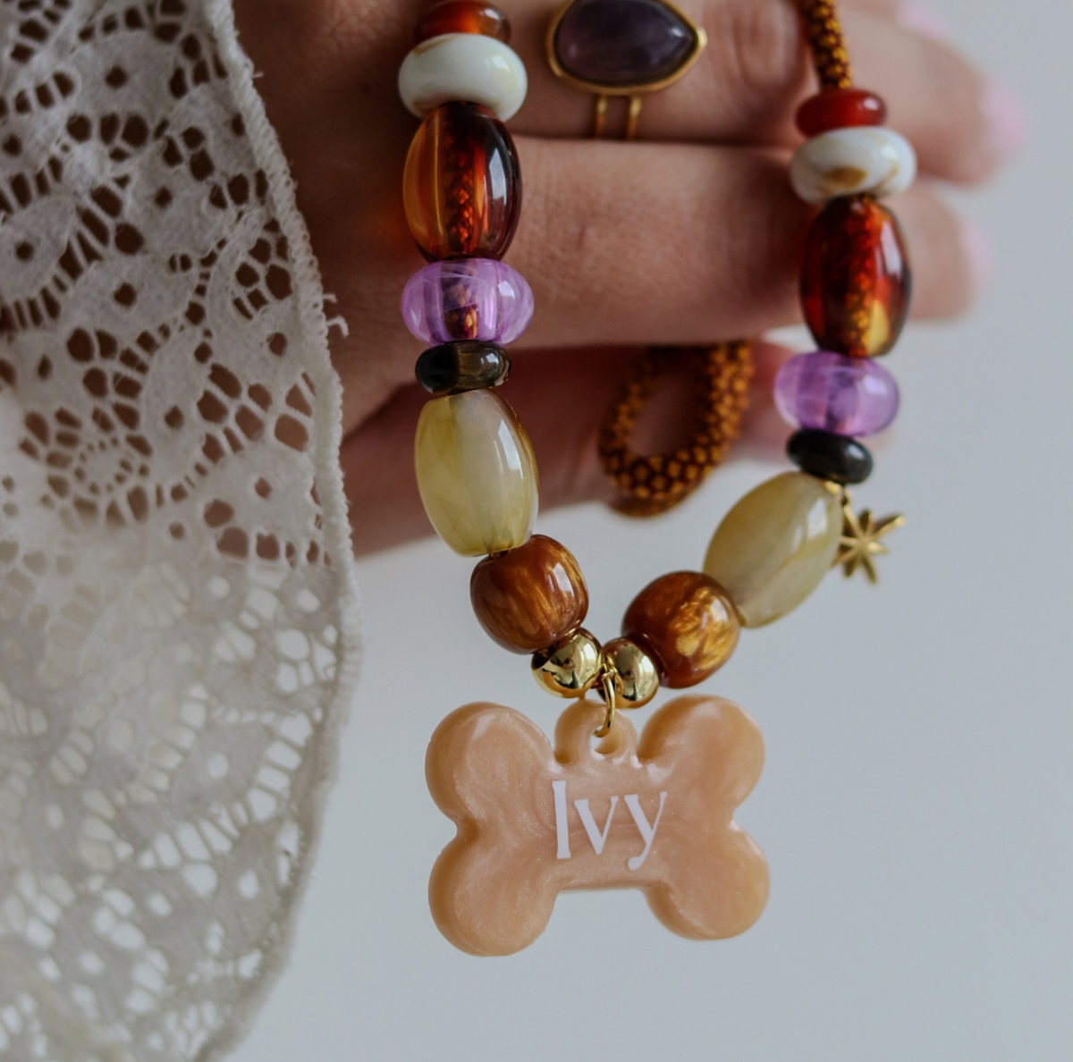 Handgemaakte hondenketting aan een roestbruin koord met amberkleurige en beige kralen, een glinsterend sterretje en een personaliseerbare botvormige naamhanger.