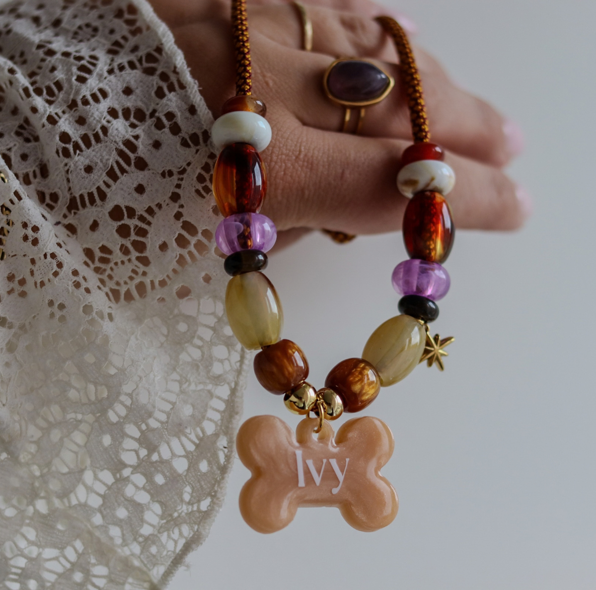 Handgemaakte hondenketting aan een roestbruin koord met amberkleurige en beige kralen, een glinsterend sterretje en een personaliseerbare botvormige naamhanger.
